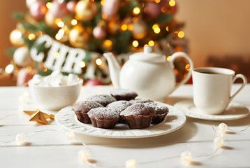 Chocolate muffins with tea on background of Christmas tree. Xmas background. Greeting card and calendar template. Christmas decoration. Holiday dinner, sweet treats for kids.