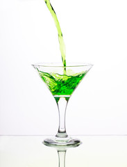 Green alcohol cocktail in martini glass with splash on white background