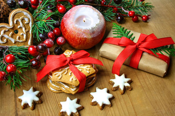 Bożonarodzeniowe tło z pierniczkami, świecą w kształcie jabłka,  prezentem, gałązkami świerku ozdobionymi czewonymi jagodami - obrazy, fototapety, plakaty