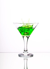 Green alcohol cocktail in martini glass with splash on white background