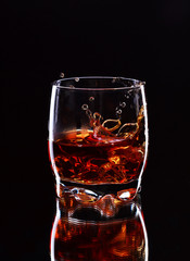 Misted glass of whiskey with splash on dark background, selective focus on the glass