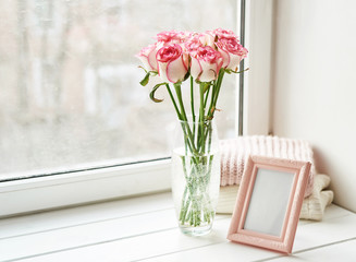 Bouquet of roses and photo frame on window. Valentine Card. Composition with fresh flowers. Space for text. Mother's day and March 8 card