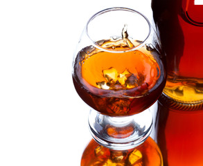 Glass and bottle of whiskey with splash on light background, selective focus on the glass