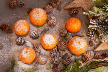 Orange tangerines on grey background in New Year's decor with brown pine cones and green leaves. Christmas decoration with mandarins. Delicious sweet clementine.