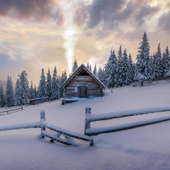 Fantastic winter landscape with wooden house in snowy mountains. Smoke comes from the chimney of snow covered hut. Christmas holiday concept