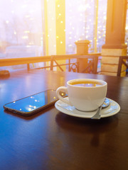 a Cup of green tea on a wooden table in a cafe. the smartphone is nearby. led lights and window in the background. bokeh. Garlands