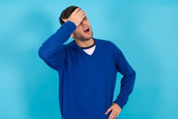 young man isolated on blue background with hands on his head