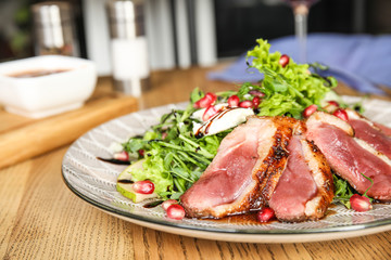 Delicious salad with roasted duck breast served on wooden table indoors, closeup