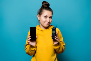 girl shows an old phone with buttons and a smartphone, restrained smiling