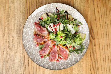 Delicious salad with roasted duck breast served on wooden table, top view