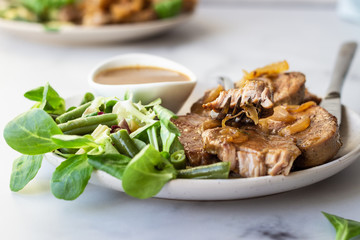 Fried juicy pork chops with caramelized onion and sauce served with green salad and beans. Light grey background, selective focus.