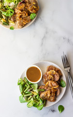 Fried juicy pork chops with caramelized onion and sauce served with green salad and beans. Light grey background, selective focus.