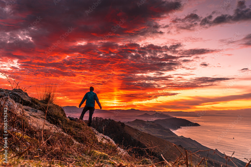 Wall mural a young man in the incredible orange sunset on the winged mount jaizkibel of san sebastian. basque c