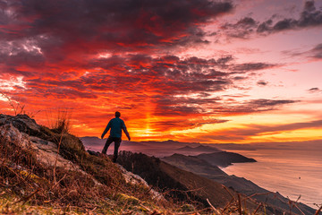 Naklejka premium A young man in the incredible orange sunset on the winged Mount Jaizkibel of San Sebastian. Basque Country