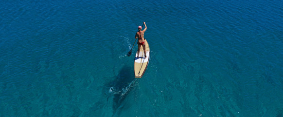 Fototapeta premium Aerial drone ultra wide panoramic photo of unidentified fit woman practising in Stand Up Paddle board or SUP in tropical island exotic turquoise bay