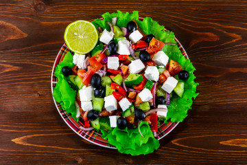 plate of tasty healthy greek salad on a blrown wooden table , national dish of Greece on a beautiful background , greek's kitchen with spices , fork and lemon