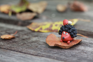 Plasticine world - small homemade hedgehog with boletus on his back surrounded by fallen autumn leaves, selective focus on the hedgehog