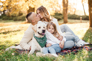 Happy beautiful family with dog labrador is having fun  are sitting on green grass in park.