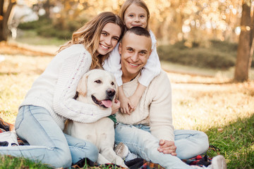 Happy beautiful family with dog labrador is having fun  are sitting on green grass in park.