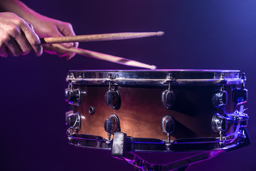 Obraz premium The drummer plays the drums. Beautiful blue and red background, with rays of light. Beautiful special effects smoke and lighting. Process of playing a musical instrument. Close-up photo.