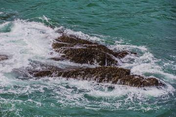 Violent energetic waves crashing on a rock in Cornwall England. Light and dark blue water foaming whilst waves break to the shore. Deep Sea Atlantic from a top a dangerous cliff