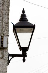 Very old style english vintage street lamp or gas lamp. victorian design in a black box with glass walls for the light to escape. Mounted on modern architecture wall in the current age