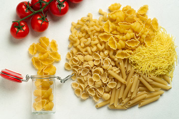 Raw pasta of different types durum wheat several different glass jar with cherry tomatoes top view