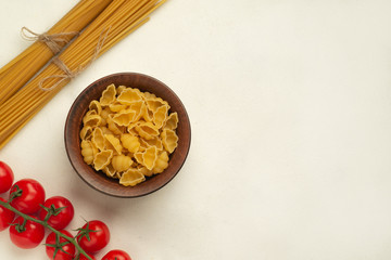 Raw pasta in a plate next to long pasta and a branch of cherry tomatoes symmetry top view free space