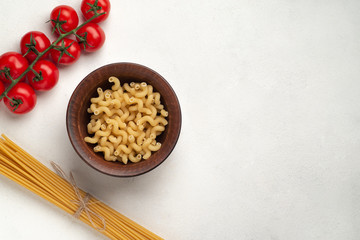 Raw long pasta and plate with curled pasta symmetry and cherry tomatoes top view free space