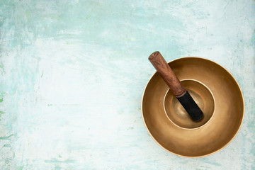 Two singing bowls stand one on the other on an artistically painted background of light blue....