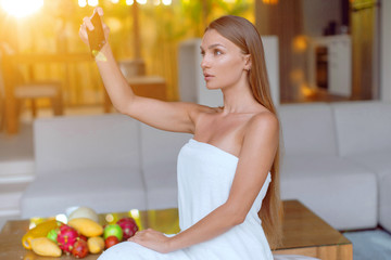 Obraz premium Young beautiful girl with a smartphone takes a selfie in the morning and talks on the Internet.
