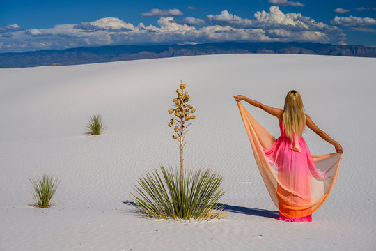 Elegant woman, wearing a fancy dress and standing like a fairy among the yuccas and dunes in the white desert