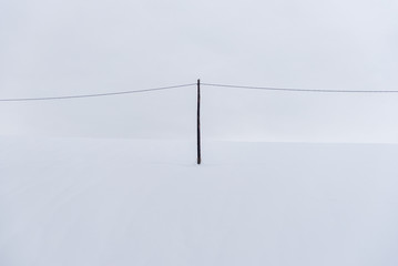 A telegraph pole standing alone on a completely snowy hill. Symmetrical composition, where the pole...