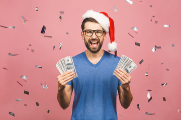 Happy Bearded man in casual and christmas hat holding money and looking at the camera isolated over...