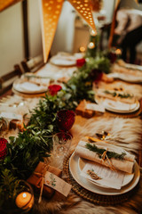 Christmas table setting for traditional lunch or dinner on a rustic table with seasonal greeting cards, tableclothes, tableware and festive decorations. Concept of family traditions and celebrations