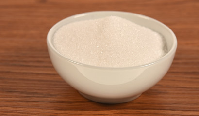 Bowl with sugar on wooden background