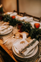 Christmas table setting for traditional lunch or dinner on a rustic table with seasonal greeting cards, tableclothes, tableware and festive decorations. Concept of family traditions and celebrations