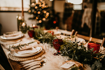 Christmas table setting for traditional lunch or dinner on a rustic table with seasonal greeting cards, tableclothes, tableware and festive decorations. Concept of family traditions and celebrations
