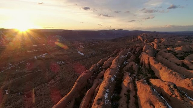 Flying backwards over desert cliffs lit up by the sun setting as the landscape glows over Moab Utah.