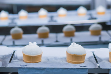Ice-cream dairy factory - conveyor belt with icecream cones at modern food processing factory. Manufacturing, dairy industry, engineering and automated technology equipment concept
