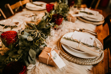 Christmas table setting for traditional lunch or dinner on a rustic table with seasonal greeting cards, tableclothes, tableware and festive decorations. Concept of family traditions and celebrations - obrazy, fototapety, plakaty