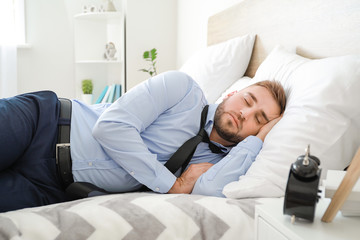 Tired businessman in formal clothes sleeping on bed