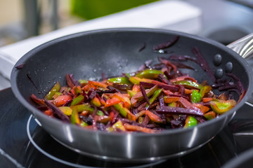 Process of cooking sliced pepper and beetroot in black frying pan with oil on electric stove at cuisine of restaurant. Professional cooking, catering, culinary, gastronomy and food concept