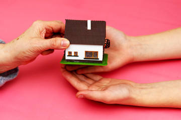 Schenkung eines Einfamilienhauses symbolisiert durch das Überreichen eines Spielzeughauses in die...