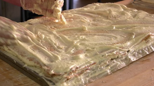 Confectioner hands decorating cake with cream. Confectioner covering cake layer with custard. Hands of the pastry chefs in the cooking process. Manufacturing process of making napoleon cake.
