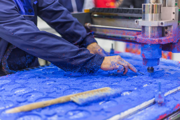 Close up view - mechanic working with milling machine. Process of cutting blue plastic sheet workpiece at automatic industrial technology exhibition. Engraving, industrial and manufacturing concept