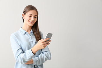 Young woman with hearing aid and mobile phone on light background