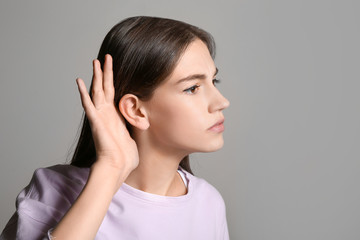 Young woman with hearing problem on grey background