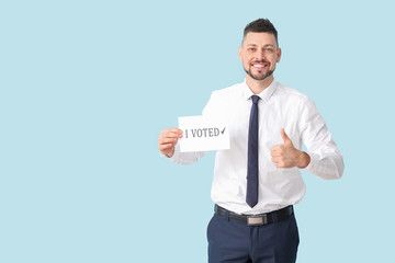 Businessman holding paper with text I VOTED and showing thumb-up on color background
