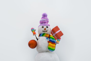 Wintertime. Hand made snowwoman with Christmas gift and New Year ball. Snowman in cap, scarf in winter. Christmas and winter fashion. Winter holidays. Merry christmas and happy new year greeting card.